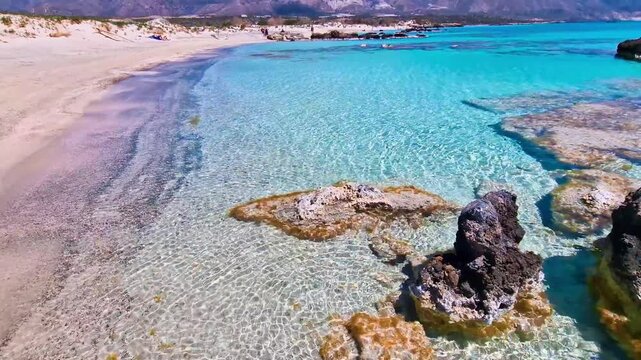 Panning view of empty iconic Elafonisi beach with pink sand and crystal clear water. Calm waves on shore, tropical transparent sea with stones underwater. Chania Crete Greece travel, 4k footage