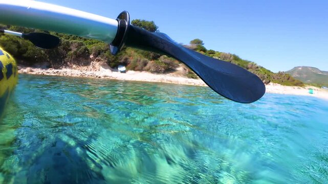 Slow motion POV of tandem kayak paddling through crystal clear water, showing synchronized strokes and ripples over a calm tropical like sea.