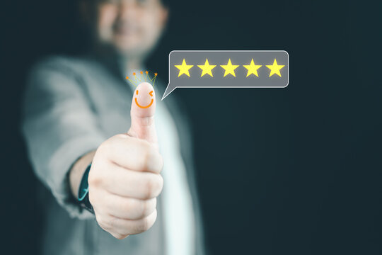 A man hand thumb up with face happy icon on the thumb and glowing yellow five stars for client the best satisfaction evaluation survey after use product and service concept.