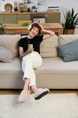 Young beautiful woman enjoys a relaxing moment at home while using her phone and smiling © LIGHTFIELD STUDIOS