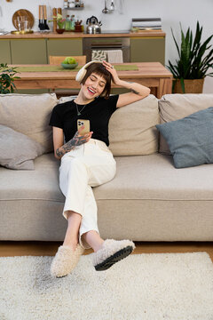 Young beautiful woman enjoys a relaxing moment at home while using her phone and smiling
