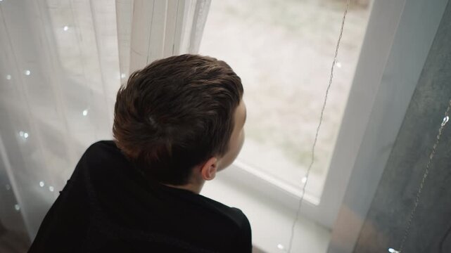 Child watches sunrise. Young child calmly views breaking dawn light. Boy peacefully gazes at first light of morning. Young boy observes sunrise with gentle curiosity and quiet admiration