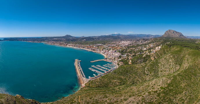 Sweeping panoramic view of Javea (Xabia), Costa Blanca, Spain, showing turquoise Mediterranean bay, marina with moored boats, town, beach and Montgo mountain