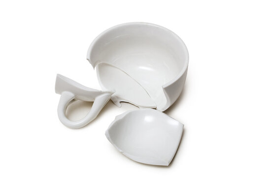 Close-up of a smashed white ceramic coffee mug or teacup lying in pieces on a clean white surface. Isolated on white with shadows.