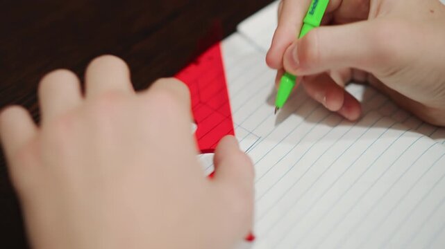 Young grandson tracing triangle with ruler, closeup hands using red set square and green pen to trace shape on lined notebook, focused concentration on geometry homework, quiet home study, gentle