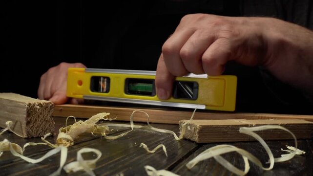 Skilled carpenter uses a level tool to ensure accuracy while measuring wooden planks on a workbench surrounded by wood shavings and tools