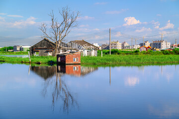 An abandoned brick house stands in a flooded field in Donggang, Chiayi, Taiwan, with its reflection visible in the calm water under a blue summer sky. © twabian