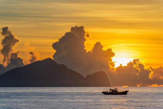 A small fishing boat sails on the ocean during a golden summer sunrise with the silhouette of Guishan Island in the background in Yilan, Taiwan.