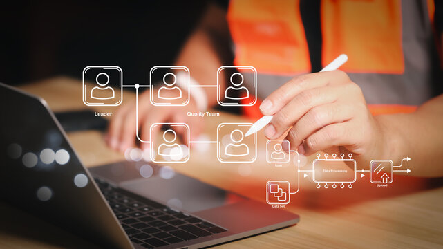 Professional engineer in safety vest using stylus pen to manage organizational chart and quality team on virtual screen via laptop for industrial human resources and project management.