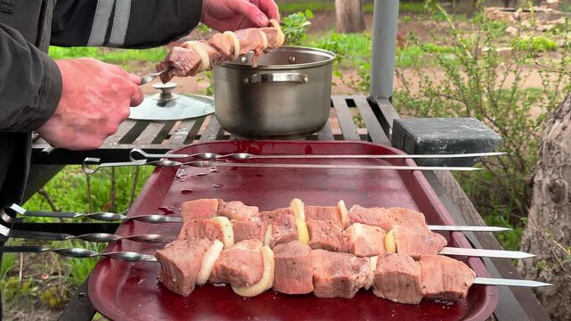Close up of preparing skewers with raw marinated meat and onions for grilling in a backyard. A tray with prepared kebabs in the foreground. Spring picnic concept