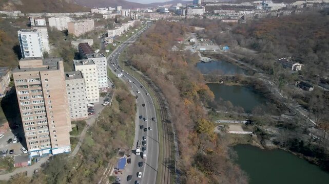 City Park in Vladivostok, showing vibrant autumn foliage and several small lakes. A road separates the park from nearby residential buildings, with the urban landscape stretching into the distance.