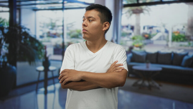 Man standing upright with arms crossed showing hands and forearms in a building lobby with visible sofa behind; confidence determination.
