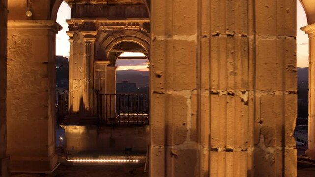 Cathedral Basilica of Immaculate Conception in Durango Mexico illuminated at twilight. Baroque stone arches frame colorful sunset sky with distant mountains and city lights below.