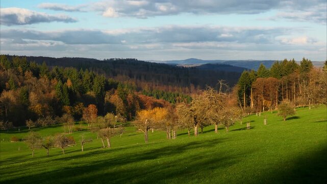 Time lapse of a picturesque rural landscape with moving clouds casting shadows on the hills, trees and meadows