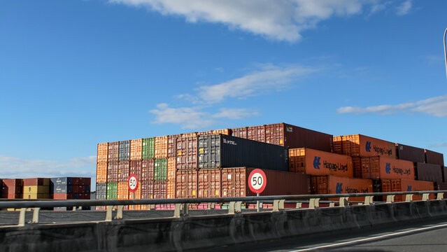 Stacked shipping containers viewed along a main route with recognizable branding from major logistics companies (Mount Maunganui, New Zealand - Mar 7, 2026). Editorial Use Only.