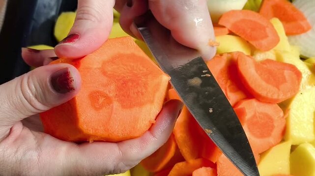 Hands use a knife to cut the carrots and add to the potatoes on a baking sheet