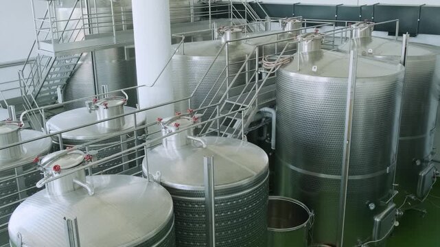 Stainless steel fermentation and storage tanks with upper walkways in modern wine production factory. Industrial wine production in Armenia. Modern winery interior. Food and beverage technology