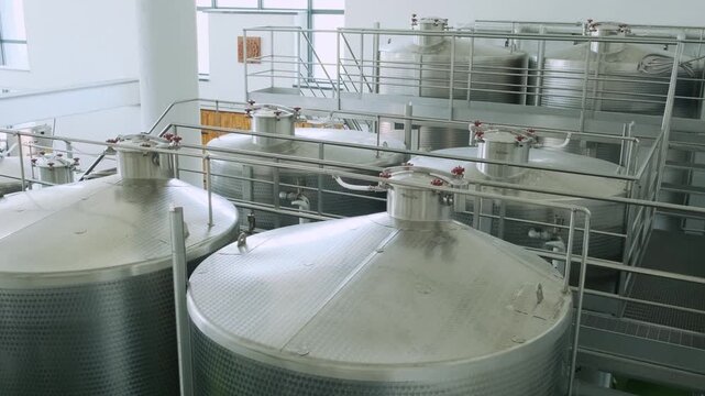 Top view of large fermentation tanks in winery facility connected with metal platforms and pipes. Industrial wine production infrastructure in modern plant. Food and beverage technology