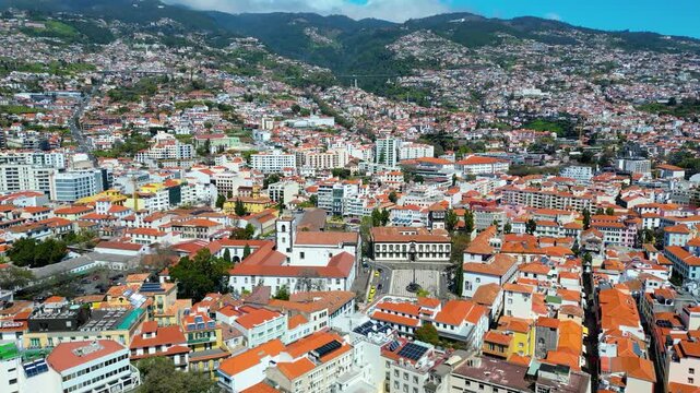 Aerial view of Funchal, Madeira, Portugal, showcasing its vibrant urban sprawl climbing lush green hills under a bright blue sky.