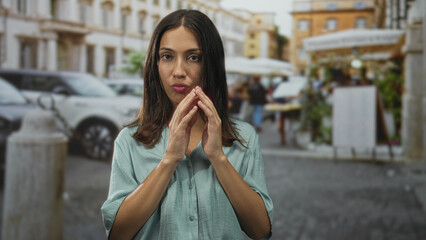 Fototapeta premium Hispanic brunette young woman blowing a kiss with both hands near mouth on a cobbled street in town; playful flirtation.