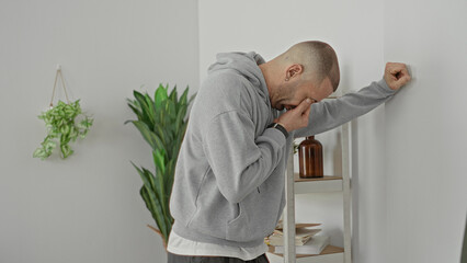 Fototapeta na wymiar Man in gray hoodie leans on shelving unit, holds frame edge and rubs eyes in building; fatigue frustration reflection.