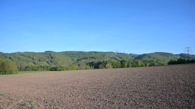 Expansive plowed field under a clear blue sky with distant forested hills