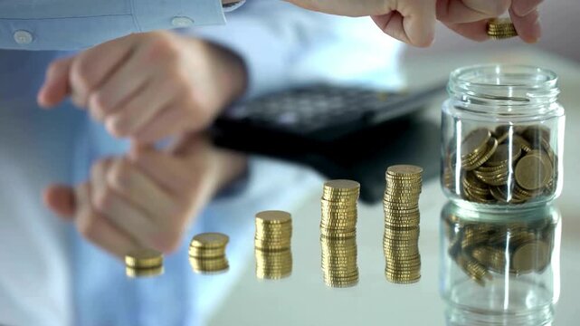 Businessman stacking gold coins on a desk with a savings jar