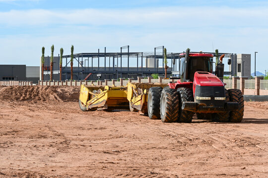 Tractor with grading attachment preparing soil at a large commercial development site, representing earthmoving, land leveling, and site preparation for construction