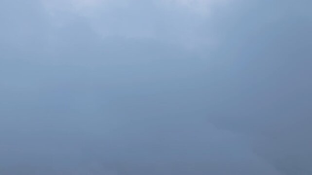 Dramatic gray storm clouds drift across an overcast sky as subtle sun rays attempt to break through the dense cloud cover. Moody atmospheric weather conditions create a cinematic cloudscape scene.