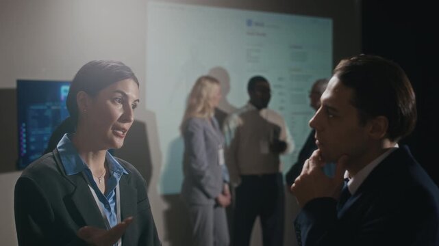 Handheld chest up shot of two Caucasian colleagues in formalwear talking at business conference, young blonde businesswoman joining conversation