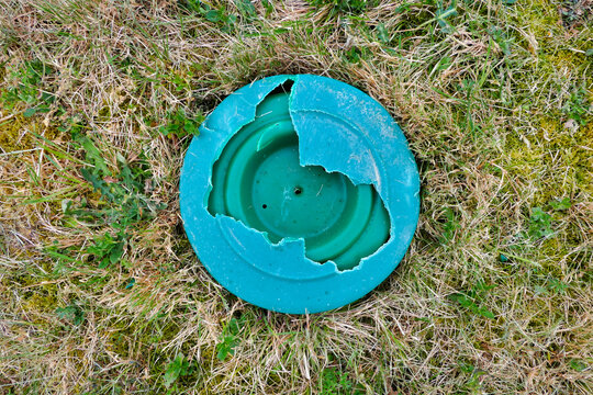 Green plastic inspection cover of a sand and gravel filter bed broken by a sit on lawnmower
