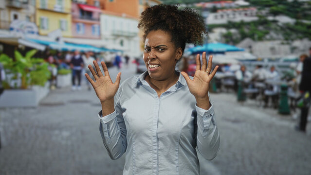 Woman with hands raised and grimacing, palms visible and recoiling slightly on a busy city street; disgust repulsion avoidance.