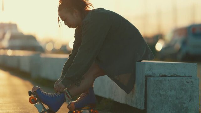 Young woman tying laces on roller skates at sunset
