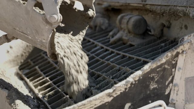Close-up view of fresh, wet concrete pouring from a mixer truck's chute into a concrete pump hopper at a construction site, showcasing the industrial building and foundation process
