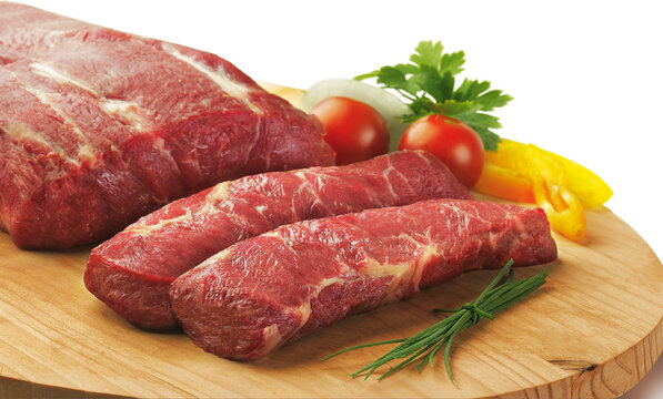 Raw flat iron steak cuts on a wooden board with fresh tomato and herbs garnish