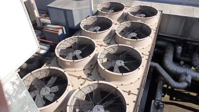 An overhead view of an old industrial chiller shows large cooling fans spinning steadily within a worn metal housing. The surfaces appear weathered and slightly rusted.