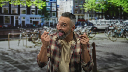 Man sticking tongue out and gesturing with hands on a city street by bicycles and a canal near buildings and trees  playful mischief. © Krakenimages.com