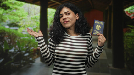 Fototapeta premium Arab woman in a striped top holds a belarus passport and waves her hand in a building corridor; travel uncertainty.