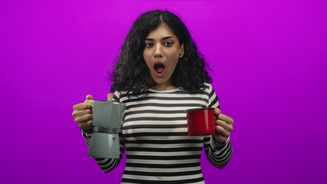 Woman brunette holding gray moka pot and red mug, mouth open in magenta studio with striped top visible; surprise.