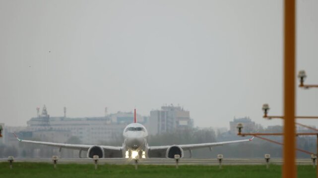 Front view white passenger aircraft taking off directly toward camera from runway, emerging from heat haze on horizon and accelerating during climb, overcast sky, navigation lights, telephoto shot