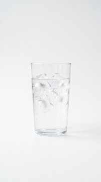 Vaso transparente con agua y cubos de hielo sobre fondo blanco, iluminaci&oacute;n suave, estilo ultra minimalista.