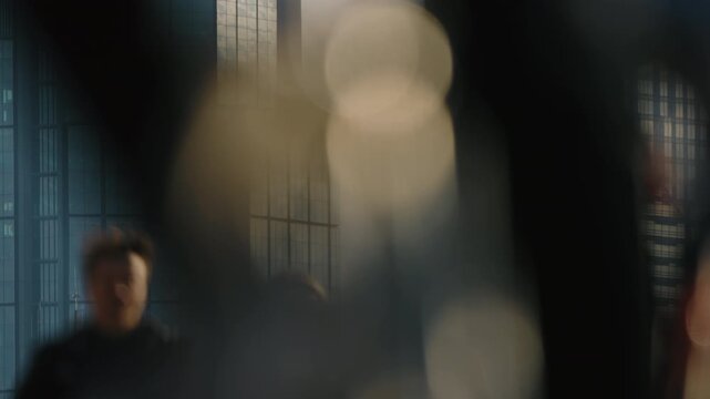 Telephoto city scene with glass skyscrapers skyline in sharp focus under soft morning or evening light, blurred pedestrians moving across pedestrian bridge in foreground, urban lifestyle in motion