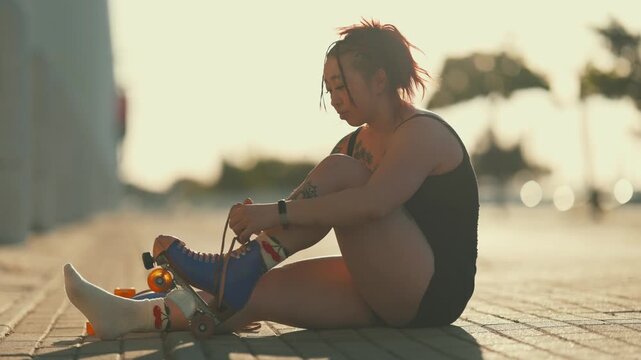 Tattooed asian woman tying roller skates in the sun