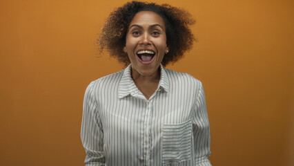 Fototapeta premium Woman clapping hands in studio with orange wall and striped shirt visible from chest up; joy celebration.