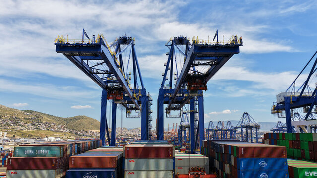 Aerial drone photo of container ship docked in terminal of port of Perama during huge cranes loading - unloading from truck size ship, Attica, Greece