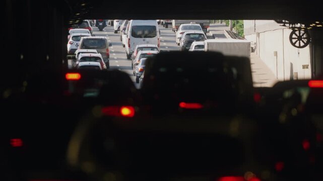 View from inside urban highway tunnel traffic jam, dark foreground filled with red brake lights, bright daylight exit in focus with compressed traffic and subtle heat haze, cinematic contrast scene