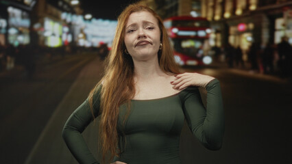 Fototapeta premium Redhead woman cups hand to ear on a busy city street at night near a red double decker bus and blurred crowd; frustration seeking help.