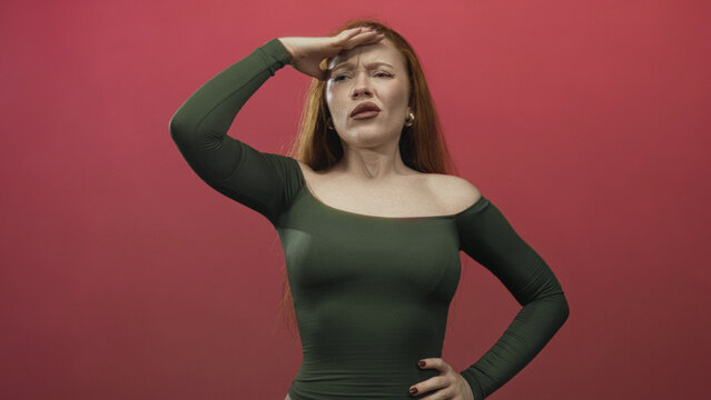 Redhead woman hand to forehead shading eyes with exposed shoulder in studio; exasperation pondering.
