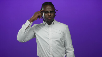 Naklejka premium Young african american man pointing finger to temple while wearing glasses and white shirt in studio purple backdrop; thoughtful.
