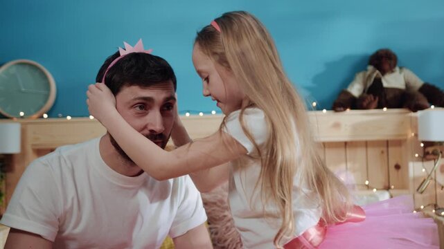 Closeup cute view young girl princess putting a crown on hher father's head. Little daughter dressing her daddy like princess for a home costume fancy party.